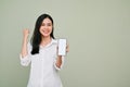 Beautiful Asian female showing a smartphone and on fist up, against grey background Royalty Free Stock Photo