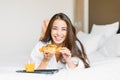 Beautiful young asian woman with long hair in white robe having breakfast croissant and orange juice in bed of hotel room Royalty Free Stock Photo