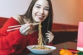 Beautiful smiling young asian woman in red clothes eating asian food with bamboo chopsticks in the chinese vietnamese restaurant