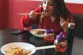 Beautiful smiling young asian woman in red clothes eating noodles with bamboo chopsticks in the chinese vietnamese restaurant Royalty Free Stock Photo