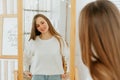 Beautiful smiling young caucasian woman with long hair, doing hair style, standing near mirror and looking at reflection Royalty Free Stock Photo