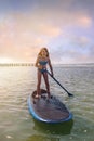 young girl doing paddle board on the beach at sunset