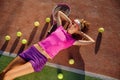 Beautiful smiling young girl in pink uniform and sporty cap lies on outdoor tennis court with a lot of balls after Royalty Free Stock Photo