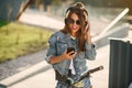 Beautiful smiling young girl wearing casual summer clothes sits on a bicycle outdoors at urban space and listens to Royalty Free Stock Photo