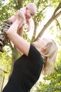 Beautiful, smiling young mother holds her baby boy up in outstretched arms.