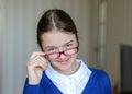 Beautiful smiling young schoolgirl in uniform looking over the top of glasses at camera, close-up. Back to school Royalty Free Stock Photo