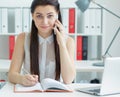 Beautiful smiling young secretary talking on the mobile phone sitting at office an looking into the camera. Business Royalty Free Stock Photo