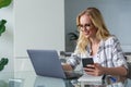 beautiful smiling young woman in eyeglasses using laptop and smartphone while working