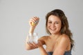 Beautiful, smiling young woman with healthy skin squeezing lemon into water against grey studio background Royalty Free Stock Photo