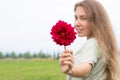 Beautiful smiling young woman holding red dahlia flower with many petals, looking and showing it at camera Royalty Free Stock Photo