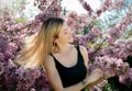 Beautiful smiling young woman near the blossoming spring tree. Portrait of pretty blond girl with long hair in pink flowers. Royalty Free Stock Photo