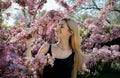 Beautiful smiling young woman near the blossoming spring tree. Portrait of pretty blond girl with long hair in pink flowers. Royalty Free Stock Photo