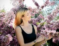 Beautiful smiling young woman near the blossoming spring tree. Portrait of pretty blond girl with long hair in pink flowers. Royalty Free Stock Photo