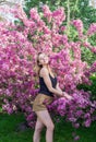 Beautiful smiling young woman near the blossoming spring tree. Portrait of pretty blond girl with long hair in pink flowers. Royalty Free Stock Photo