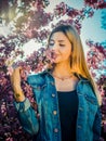 Beautiful smiling young woman near the blossoming spring tree. Portrait of pretty blond girl with long hair in pink flowers. Royalty Free Stock Photo