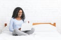 Beautiful smiling young woman sitting on bed, using laptop Royalty Free Stock Photo