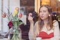 Beautiful smiling young woman sitting in coffee shop near the window,drining coffee and eating dessert