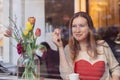 Beautiful smiling young woman sitting in coffee shop near the window,drining coffee and eating dessert