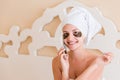 Beautiful smiling young woman with under eye patches and talking mobile phone in bathrobe sitting in bed. Happy girl taking care Royalty Free Stock Photo