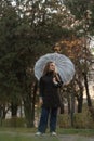 Beautiful smiling young woman under transparent umbrella in autumn park. Girl in black coat walks on the rain Royalty Free Stock Photo