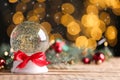Beautiful snow globe and Christmas decor on wooden table against blurred festive lights, space for text. Bokeh effect Royalty Free Stock Photo