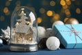 Beautiful snow globe, gift box and Christmas decor on blue table against blurred festive lights Royalty Free Stock Photo