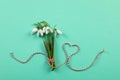 Beautiful snowdrops with traditional cord martisor on turquoise background, flat lay. Symbol of first spring day