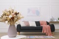 Beautiful sofa with cushions and bouquet in living room, focus on flowers. Interior design