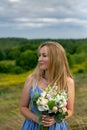 Vertical close-up portrait of a beautiful thirty-five year old blonde with a bouquet against the backdrop of a summer landscape Royalty Free Stock Photo