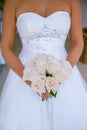 Beautiful, sophisticated bride wearing a ballgown style dress and holding a round pink roses bouquet,