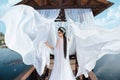 A beautiful sorceress stands on the background of a wooden gazebo by the water, with a white air dress. In the picture