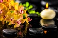 beautiful spa composition of blooming twig orange orchid flower, green foliage with water drops, candle and zen basalt stones, cl Royalty Free Stock Photo