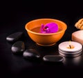 Beautiful spa composition with pink orchid on cup, stones and white gloves on black wooden table Royalty Free Stock Photo