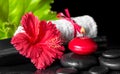 beautiful spa composition of red hibiscus flower with dew, candles, green leaf and rolled towel tied with ribbon on zen stones Royalty Free Stock Photo