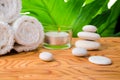 Beautiful spa setting of stones, candle, rolled white towels and green leaf on root wood background
