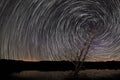 Beautiful Spiral Star Trails over lake with old tree.