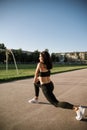 A beautiful sports girl in black sportswear is doing a warm-up at the stadium. The concept of a healthy lifestyle