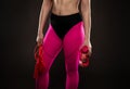 A beautiful sportswoman in leggings holds a bottle of water and a red jump rope in her hands in the gym