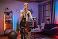 Beautiful sporty fit female cycling stationary bike and watching online fitness class on smartphone. Royalty Free Stock Photo