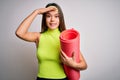 Beautiful sporty girl doing sport wearing sportswear holding yoga mat over white background stressed with hand on head, shocked Royalty Free Stock Photo