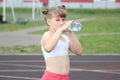 A sporty girl drinks water from a bottle and smiles sweetly at a running stadium Royalty Free Stock Photo