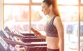 Beautiful sporty girl with earphones and smartphone walking or running on treadmill at gym Royalty Free Stock Photo