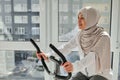 Beautiful sporty Muslim woman in hijab cycling a bike at home. Cardio training, exercising legs, Cardio workout at home Royalty Free Stock Photo