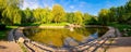 A beautiful  spring landscape with a lake in the park, surrounded by green foliage of trees in the sunlight and a stone path in Royalty Free Stock Photo