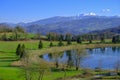 Beautiful spring landscape with mountain lake and mountains covered with snow across blue sky. Fir trees, and trees reflected in w Royalty Free Stock Photo