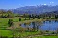 Beautiful spring landscape with mountain lake and mountains covered with snow across blue sky. Fir trees, and trees reflected in w Royalty Free Stock Photo