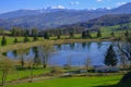 Beautiful spring landscape with mountain lake and mountains covered with snow across blue sky. Fir trees, and trees reflected in w Royalty Free Stock Photo