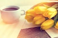 Beautiful spring music background. Cup of coffee, yellow tulips, musical page on a dark wooden background. Shallow depth of field