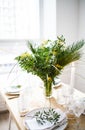 Beautiful springtime table setting with green leaves and mimosa branches, bright white table dinner decoration