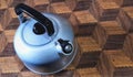 A beautiful stainless steel kettle on a tablecloth with a brown checkered pattern seen from above
